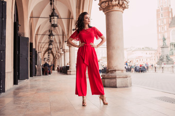 Fototapeta na wymiar Photo of beautiful stylish brunette woman in the city ,wearing red jumpsuit. Fashion summer photo