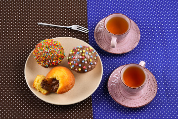 Baking with tea and chocolate on the table.  Two cups of tea with cupcakes and chocolate with a multicolored powder on the table.