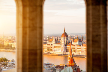 Naklejka premium Cityscape view trhough the arch on the famous Parliament building during the sunset light in Budapest, Hungary