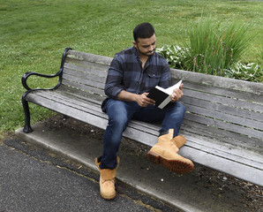 young man reading book on park bench