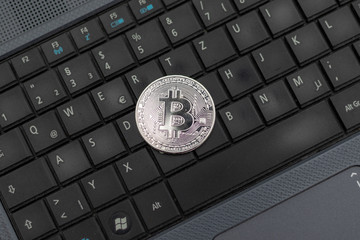 Silver bitcoin coin lying on the keyboard of a laptop 