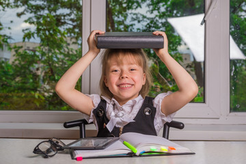 Beautiful schoolgirl siting at a desk and holding a book on the head, free space.