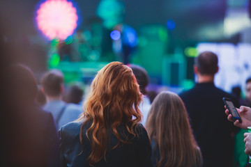 A crowded concert hall with scene stage lights, rock show performance, with people silhouette and hand holding smartphone