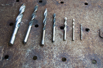 Drills of different diameters lie on a rusty sheet of metal