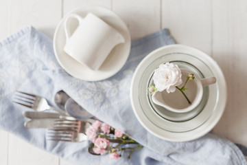 Clean glass and ceramic dishes with roses on a white wooden table. Preparing for breakfast. Soft focus.