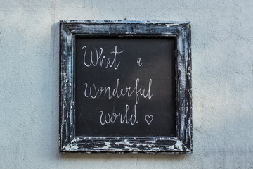 handmade wooden black vintage plate with "what a wonderful world" inscription on concrete wall concept