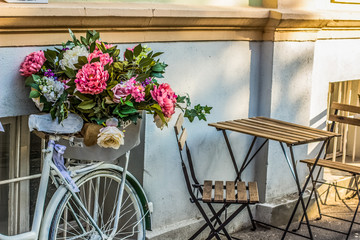 vintage bicycle with flowers and ribbon with "vintage world" inscription  near cafe and wooden table and chairs on street in summer time