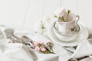 Clean glass and ceramic dishes with roses on a white wooden table. Preparing for breakfast. Soft focus.