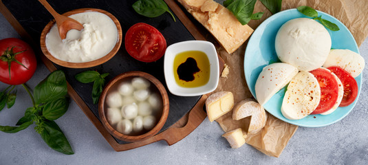 Italian cheeses. Mozzarella Buffalo, crottin, balls, Stracciatella, basil leaves, tomatoes, olive oil with vinegar on gray background. Top view, copy space.