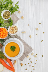 Pumpkin cream soup with croutons, raw fresh pumpkin pieces and herbs on a white rustic wooden background, Autumn concept. 