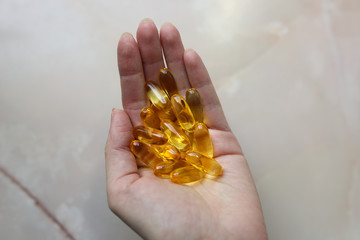Omega 3 pills in woman's hand on marble background. Healthy diet supplements. Fish oils for vegans...