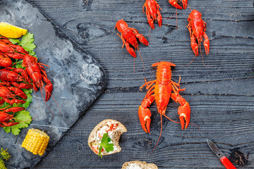 Red boiled crayfish with lemon, corn and parsley on stone slate tray on dark old rustic background © jarvna