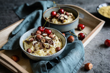 Millet porridge topped with chocolate pieces, hazelnuts, almond slices and cherry
