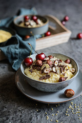 Millet porridge topped with chocolate pieces, hazelnuts, almond slices and cherry