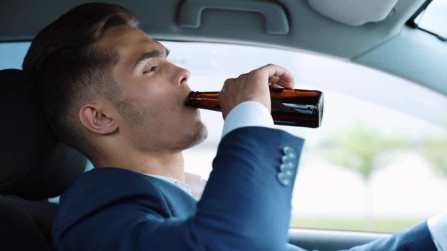 Young businessman drinking beer in car. A man in a bad mood due to a bad deal or a bad news. Drunk driver behind the wheel. Drunk, drive and unsuccessful business concept