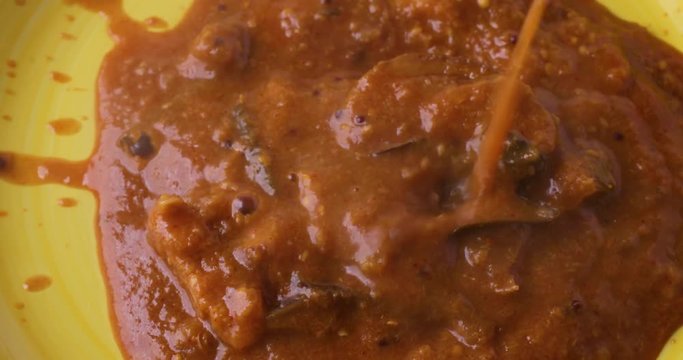 Close video of pouring hot eggplant curry onto a bright yellow plate.