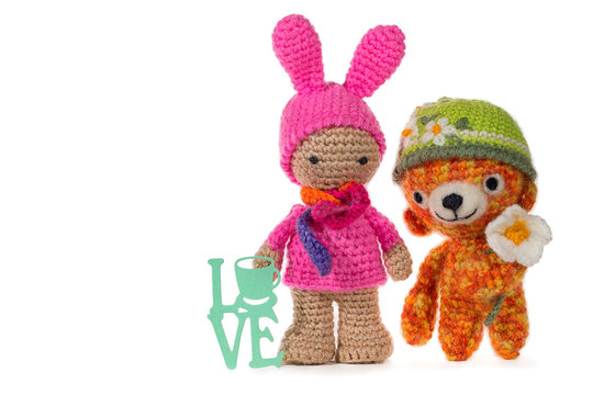 Dressed as a bunny crochet girl and crochet bear wearing a hat with a flower with sign LOVE, on white background. Amigurumi. Handmade