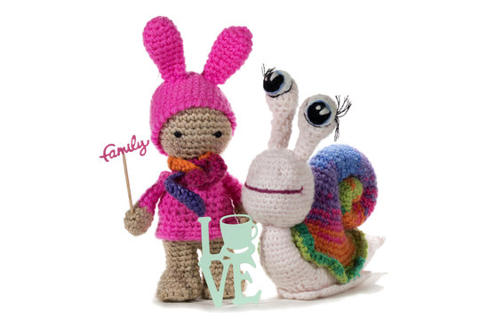 Crochet girl holding sign FAMILY and crochet rainbow snail by sign LOVE, on white background. Amigurumi. Handmade