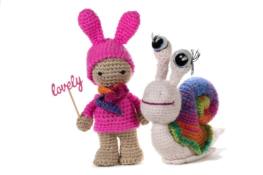 Crochet girl holding sign LOVELY and crochet rainbow snail, on white background. Amigurumi. Handmade