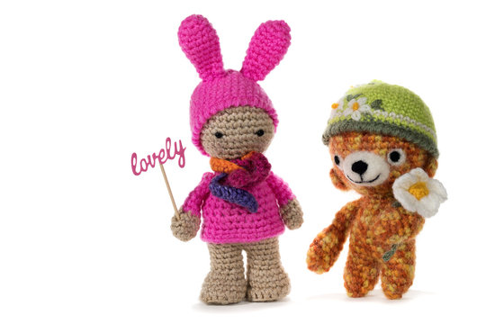 Crochet girl holding sign LOVELY and crochet bear wearing a hat with a flower, on white background. Amigurumi. Handmade