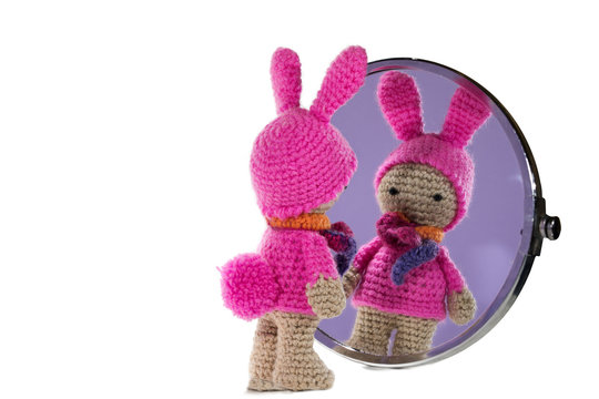 Dressed as a bunny crochet girl looking in the mirror, on white background. Amigurumi. Handmade