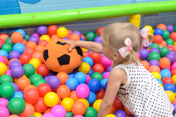 A girl in the playroom, where there are a lot of colored balls.