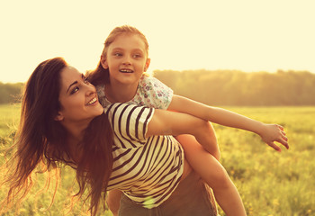 Flying kid girl laughing on the happy enjoying mother back on sunset bright summer background. Closeup toned color bright portrait.