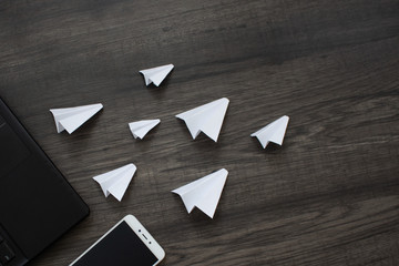 White paper planes and gadgets on a wooden background. Visual communication scheme through...