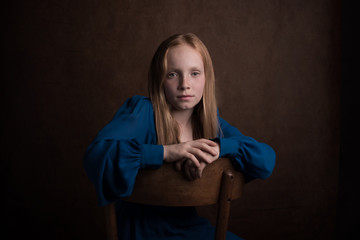 Classic studio portrait of girl in blue dress sitting on chair