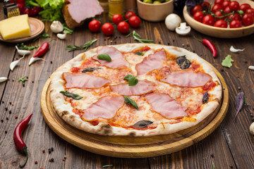 Delicious italian pizza with ham and basil leaves on wooden background