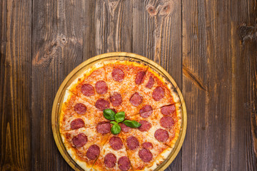 Pizza pepperoni with mozzarella cheese, salami and arugula on wooden background