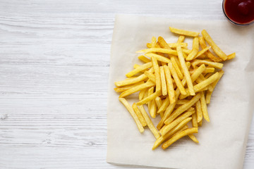 Tasty french fries with ketchup over white wooden background, top view. Space for text.