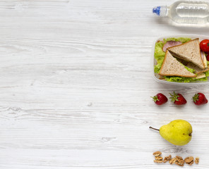 Healthy school lunch box with fresh fruits, walnuts, organic vegetables sandwiches and bottle of water on white wooden surface, flat lay. From above. Top view. Copy space.