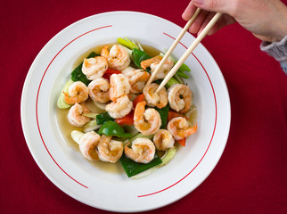 Top view of king prawns dish with onion, green and red bell peppers and hand of woman with chopsticks taking a prawn. Chinese seafood plate. Restaurant meal concept