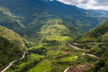 Aerial drone view of huge rice terraces in a valley surrounded by tall mountains and low hanging cloud (Banaue)