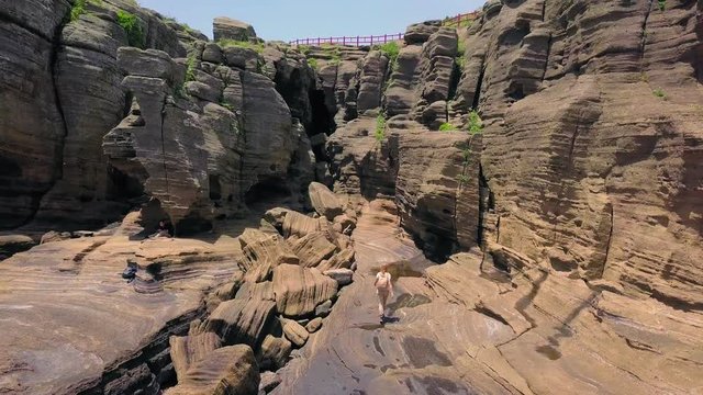 Aerial View of Young Female Traveler Walking at Aerial View of Yongmeori Coastal Walk on Jeju Island, South Korea. Rough Geological Formation Made with Erosion