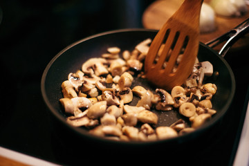 A woman is frying mushrooms and carrots. The cooking process.