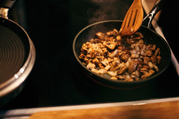 A woman is frying mushrooms and carrots. The cooking process.