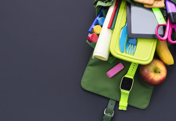 Backpack with school supplies on black background.