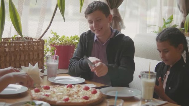 boy teen and girls eats pizza in cafe slow motion video. children eat pizza a delicious pizza. company of people friends lifestyle eating in a cafe. kids eating pizza lifestyle concept