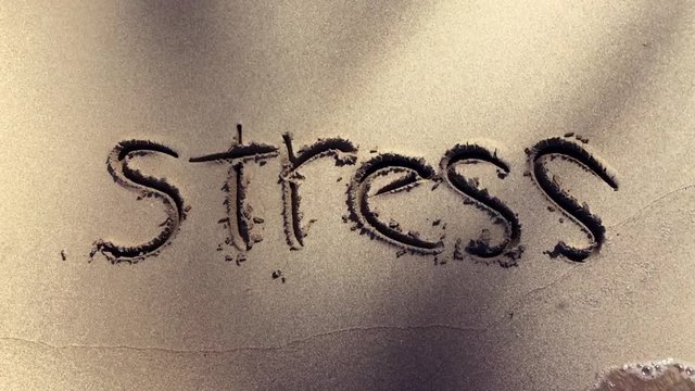 Stress handwritten in the sand washed away by a slow motion wave