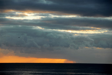 sun setting behind dark clouds over orange sky above dark sea