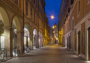 Fototapeta na wymiar Modena - Via Roma street and the Military academy in the background at dusk.