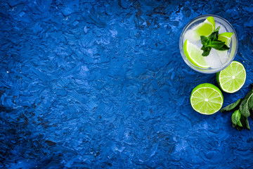 Fototapeta na wymiar Tropical cocktail. Beverage which women likes. Glass of mojito with slices of lime, mint, ice cubes on blue background top view copy space