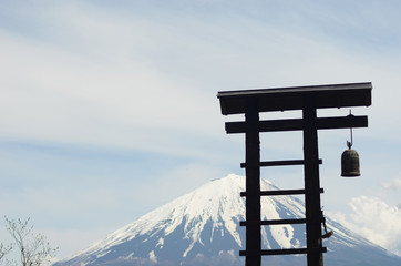 A bell tower silhouetted against Mt Fuji. The mountain is covered with snow. The sky is overcast.