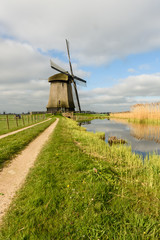 Windmill stands next to a canal in the countryside with a path leading to it in West Friesland, Netherlands
