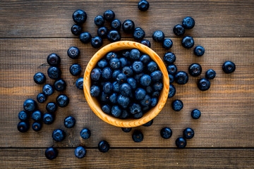 Fresh recently picked blueberries in bowl on dark wooden background top view