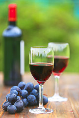 Two glasses Red Wine with wine bottle and fresh grapes on wooden table, defocused green outdoors background 6