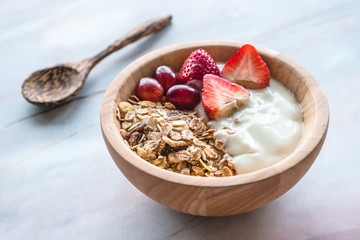 Healthy breakfast. Bowl of homemade muesli with yogurt and fresh fruits on marble table.