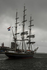 Fototapeta na wymiar A three-masted modern luxury clipper with historical nineteenth century styling sailing in the North Sea Canal's mouth under the cloudy gray sky, IJmuiden, the Netherlands.